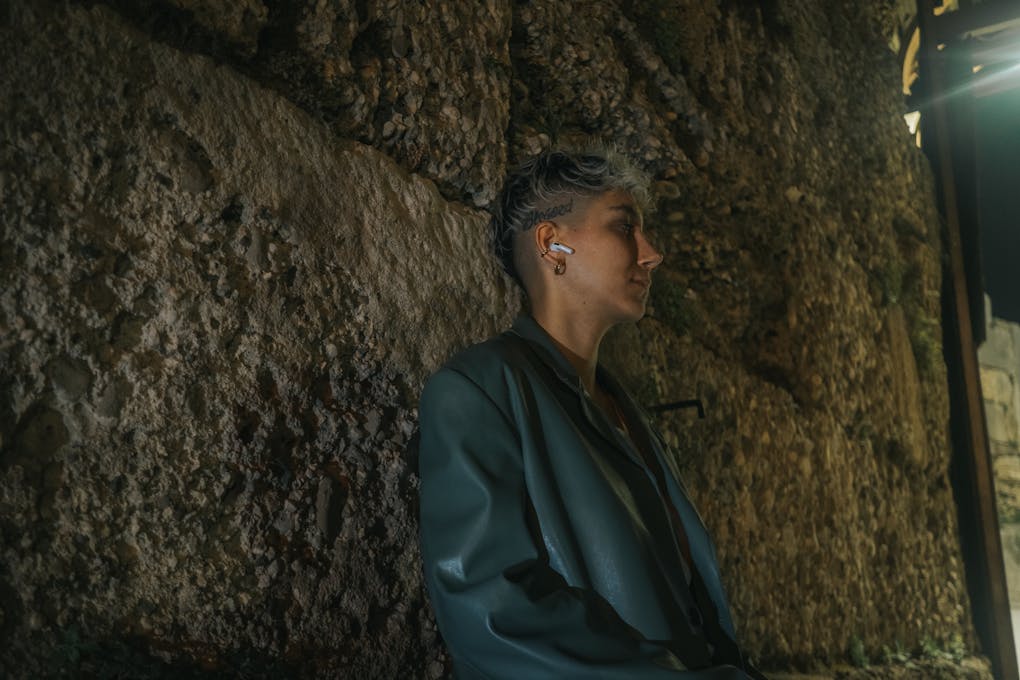 A woman in a jacket and headphones is standing by a wall